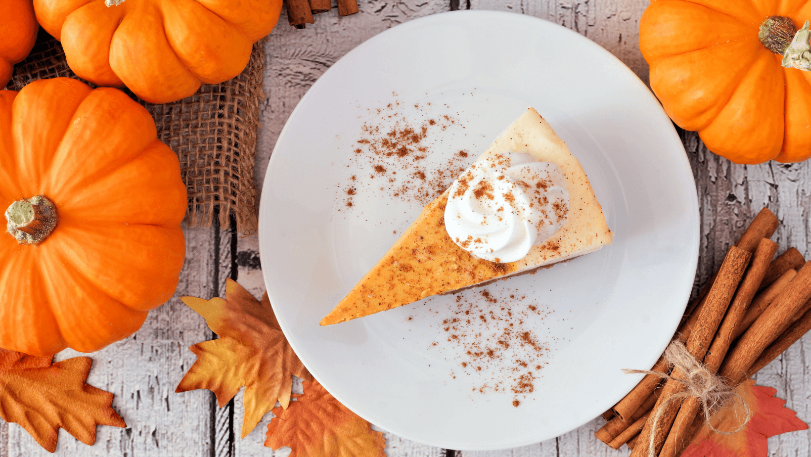 Slice of pumpkin cheesecake with whipped cream, overhead table scene on a white wood background